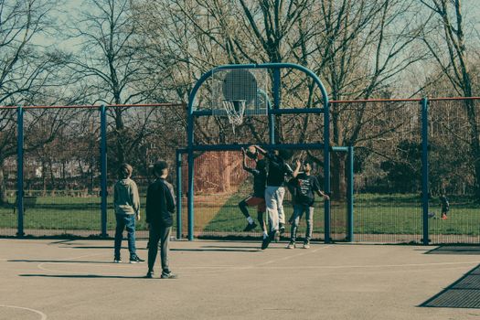 A group of teenagers playing an outdoor basketball game in an urban park setting.