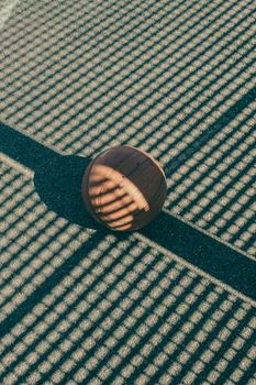 A basketball rests on sunlit pavement with strong shadow patterns, captured from above.