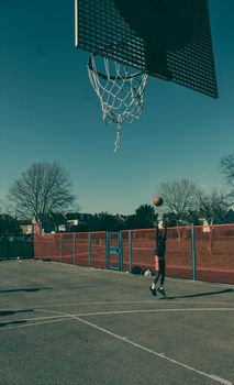 A teenager practicing basketball on an outdoor court, aiming for the hoop.