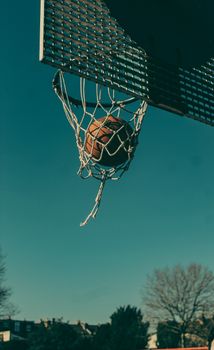 Close-up of a basketball swishing through a hoop under a clear blue sky.