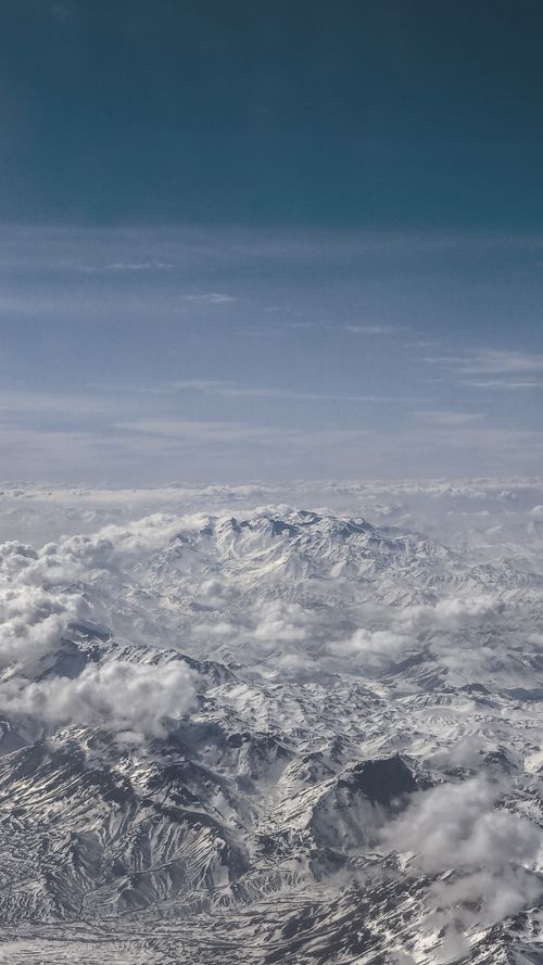 Free Breathtaking aerial view of a snow-covered mountain range with clouds. Stock Photo