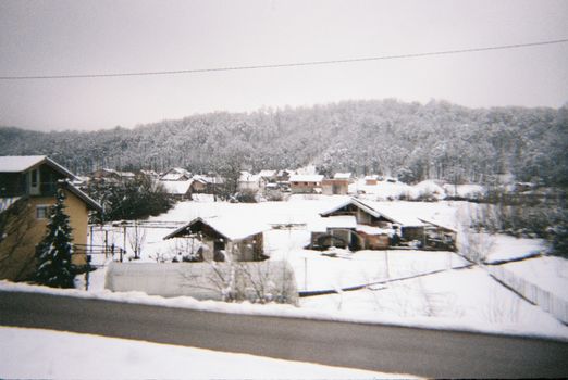 Charming village landscape covered in snow with trees and hills under a winter sky.