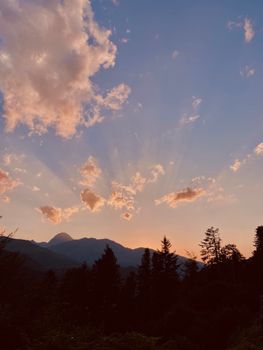 Stunning sunrise over mountain peaks with radiant light and silhouetted trees in a tranquil forest setting.