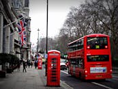 在伦敦的经典场景中，繁忙的城市街道上停着一辆红色双层巴士，旁边还有一个标志性的电话亭