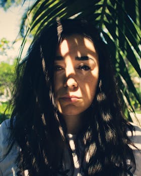 这幅肖像引人注目，描绘了一位脸上映着棕榈叶阴影的女人