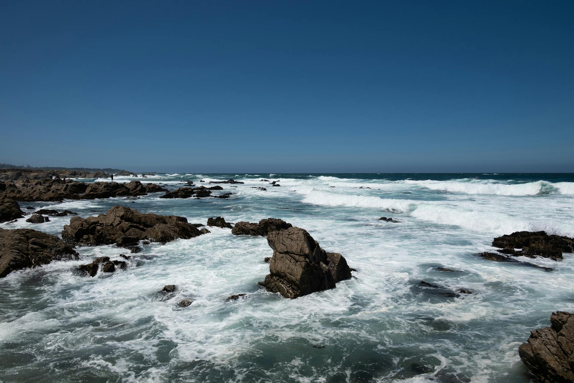 Stunning California coast with crashing waves and rugged rocks under clear blue skies.