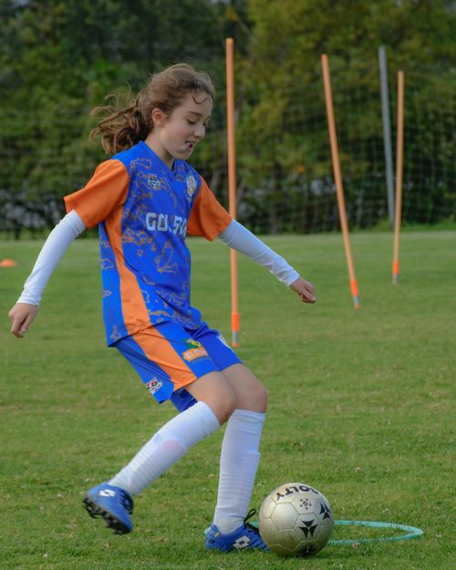 Free A young girl in sportswear playing soccer on a grass field with training equipment. Stock Photo