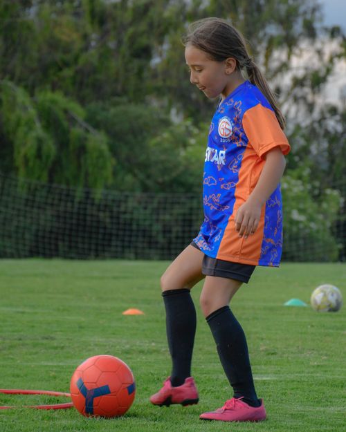 Free A young girl in sportswear practicing her soccer skills on a grassy field. Stock Photo