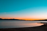 宁静的湖面上映照着宁静的日落，天空呈现柔和的渐变，远处是连绵的山丘