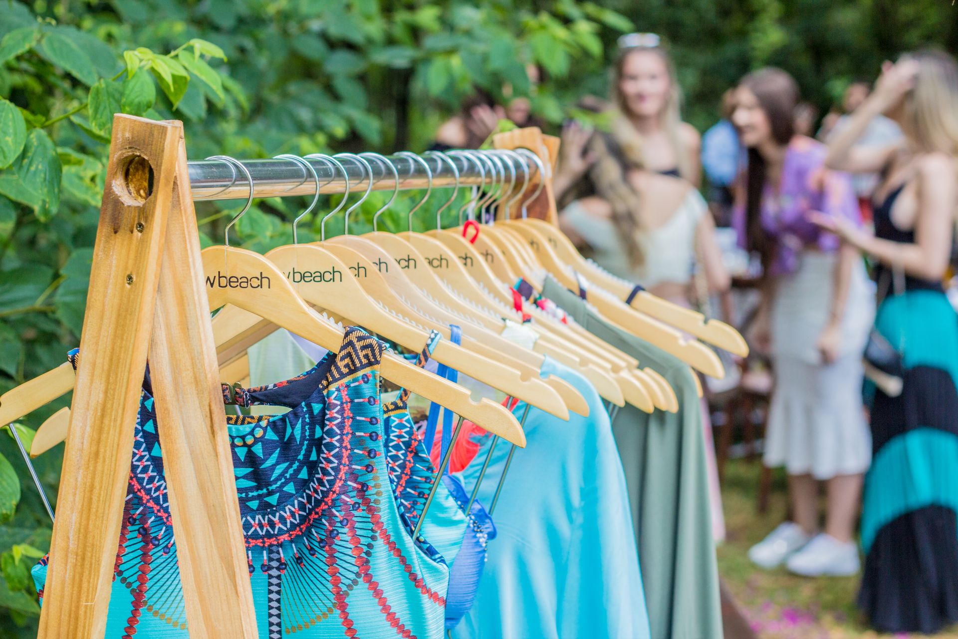 Colorful summer clothes on a rack with people socializing in a lush outdoor setting.