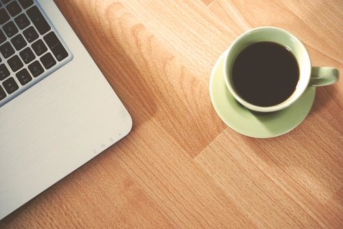 Free A coffee cup and laptop on a wooden desk, creating a cozy workspace vibe. Stock Photo