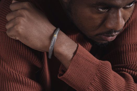 Close-up of a man with a stylish bracelet on his wrist, wearing a brown sweater.