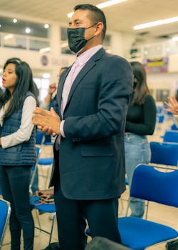 A man in a suit wearing a face mask stands attentively indoors, emphasizing professionalism and safety.