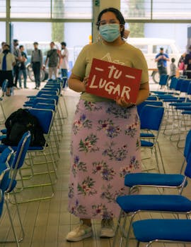 A woman holds a 'Tu Lugar' sign at an indoor event with rows of chairs.