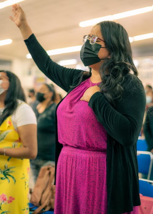 Woman in a Face Mask Standing in the Audience with Arm Raised and Eyes Closed