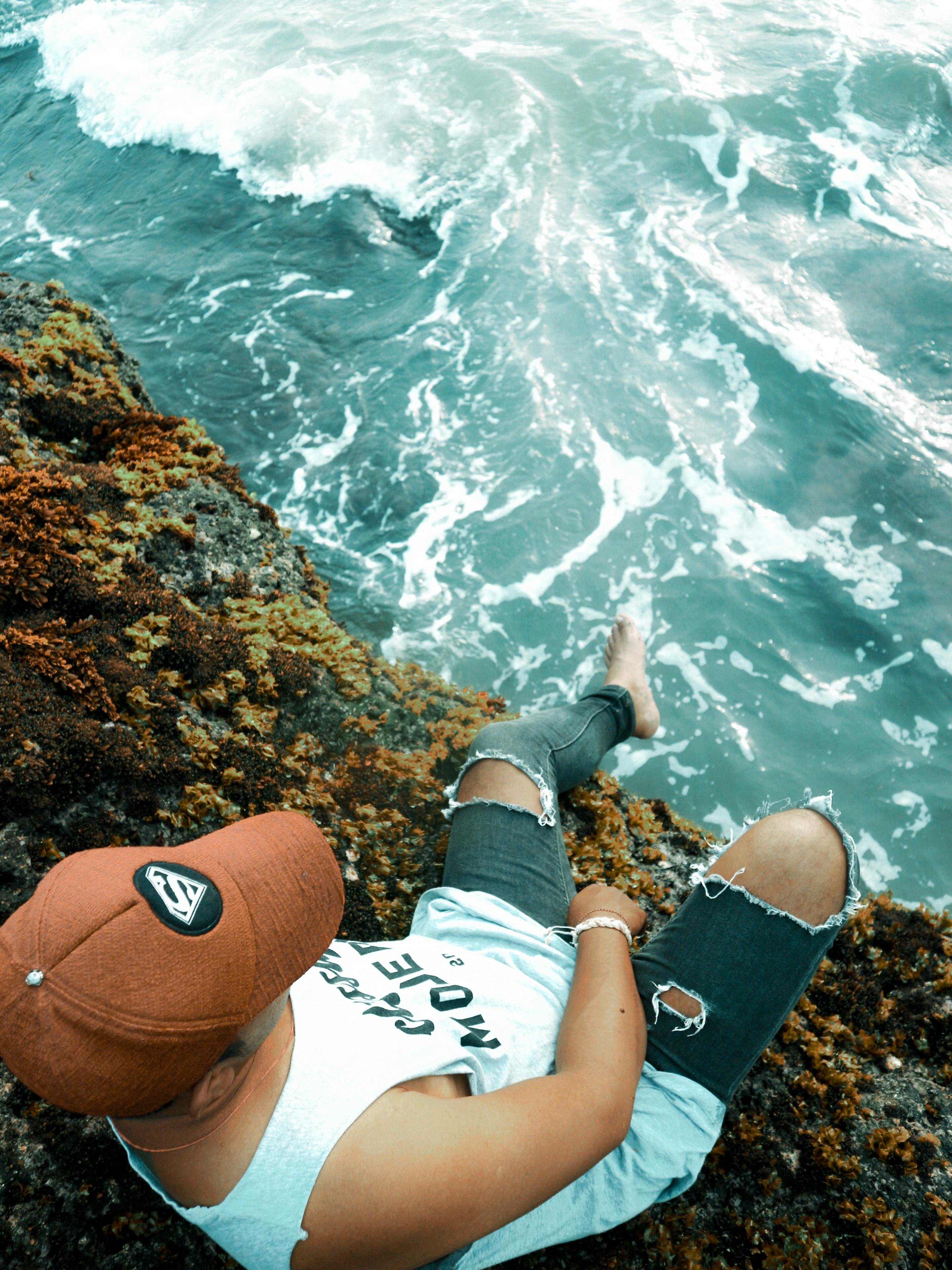 一名男子穿着休闲装，坐在岩石悬崖上，平静地凝视着下方的海浪