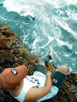 一名男子穿着休闲装，坐在岩石悬崖上，平静地凝视着下方的海浪