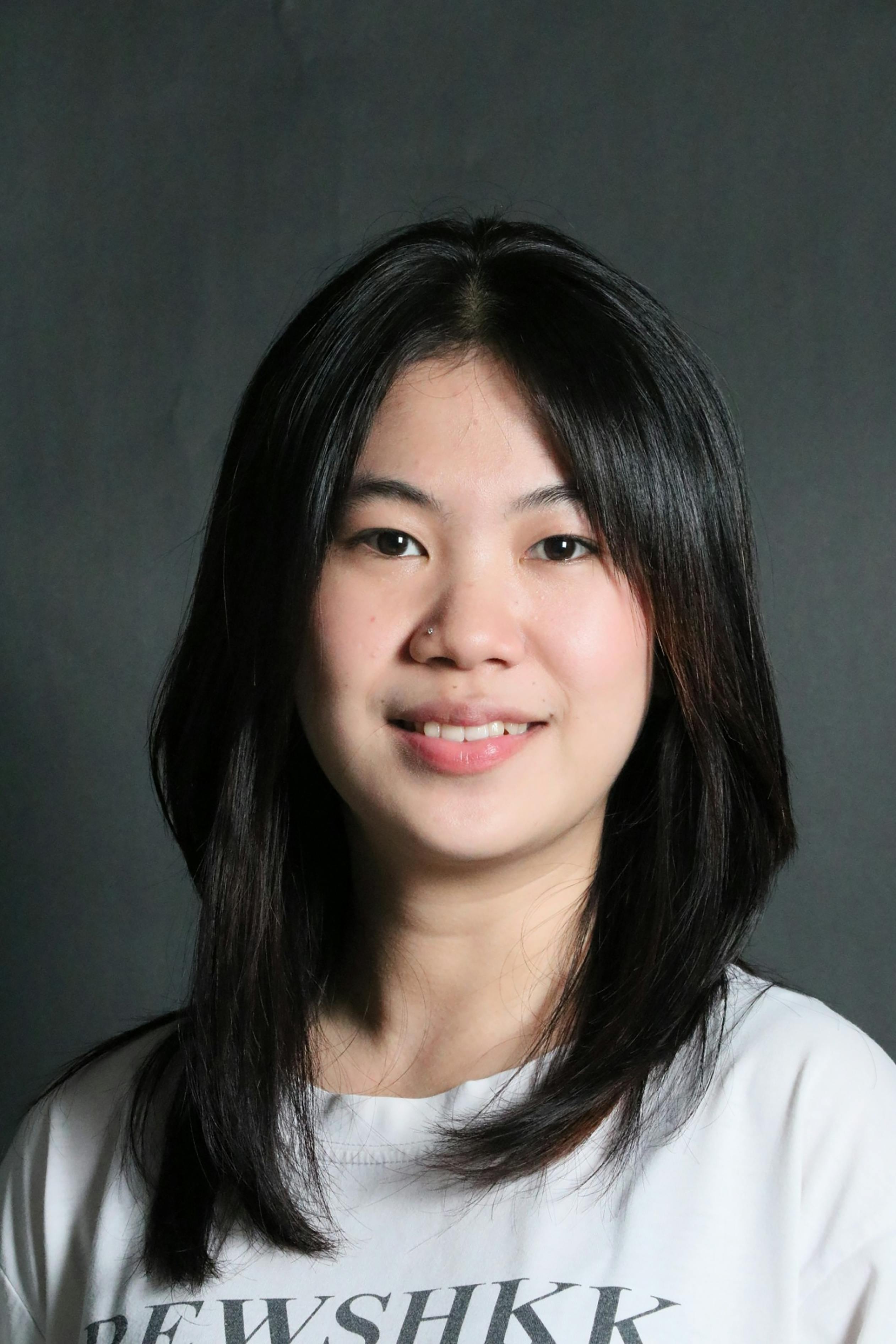 A cheerful woman with long black hair smiling in a studio portrait with a dark backdrop.