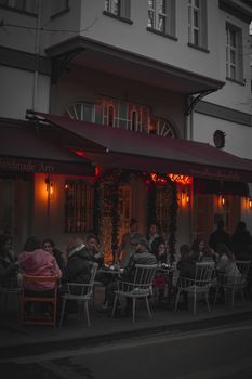 A street café scene with people enjoying an evening gathering under warm lights.