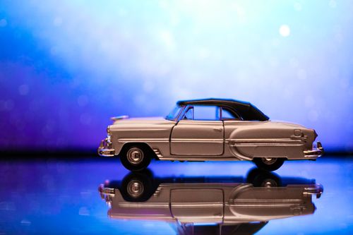 Free A classic vintage toy car captured against a shiny blue background, reflecting on a glass surface. Stock Photo