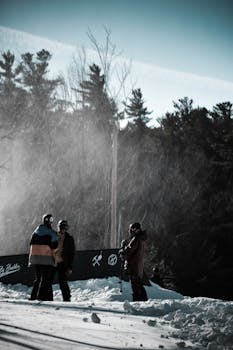 Group of snowboarders standing in snow, chatting in a winter landscape with trees in the background.