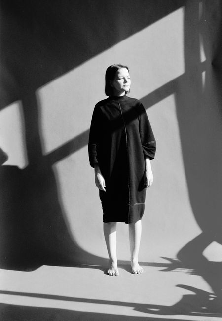 Black and white studio portrait of a woman in a minimalist dress with dramatic shadows.