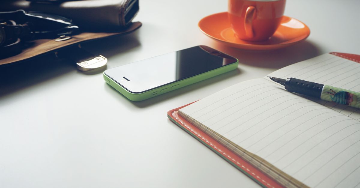 a worn leather journal open on a wooden desk with a coffee cup and a small cross beside it