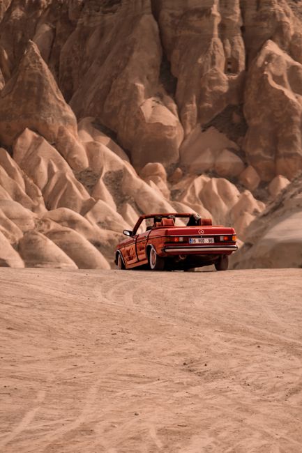 Red convertible car driving through Cappadocia's unique rocky terrain in Nevşehir, Türkiye.