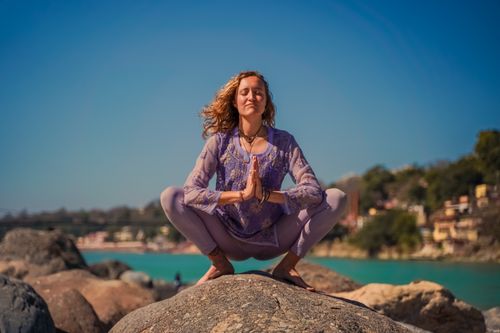 Free A woman practicing yoga on rocks in Rishikesh with a serene backdrop. Stock Photo