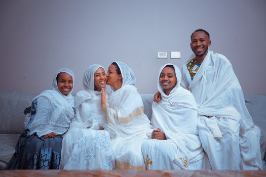 Group portrait of friends in traditional white clothing, smiling and embracing indoors.