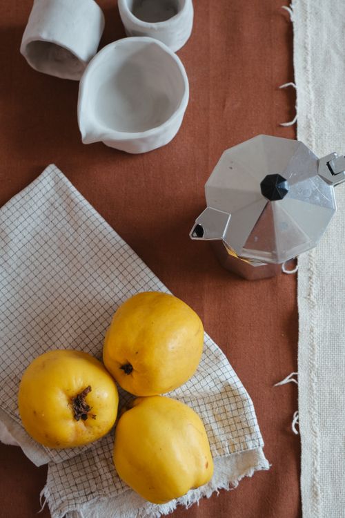 Free Artistic still life with quince fruits, moka pot, and ceramics on cloth. Stock Photo