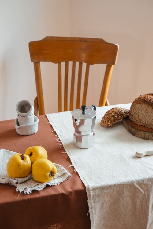Free Rustic breakfast scene with bread, fruit, and coffee pot on a wooden table. Stock Photo
