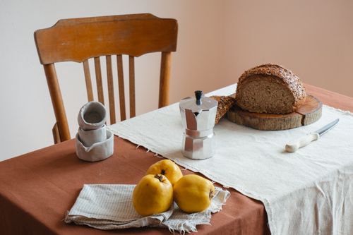 Free Rustic breakfast setup with fresh bread, quince, and a moka pot on a clothed table. Stock Photo