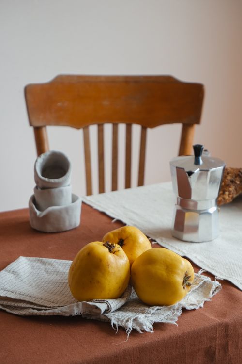 Free Charming kitchen scene with ripe quinces, a moka pot, and folded napkins on a rustic table. Stock Photo