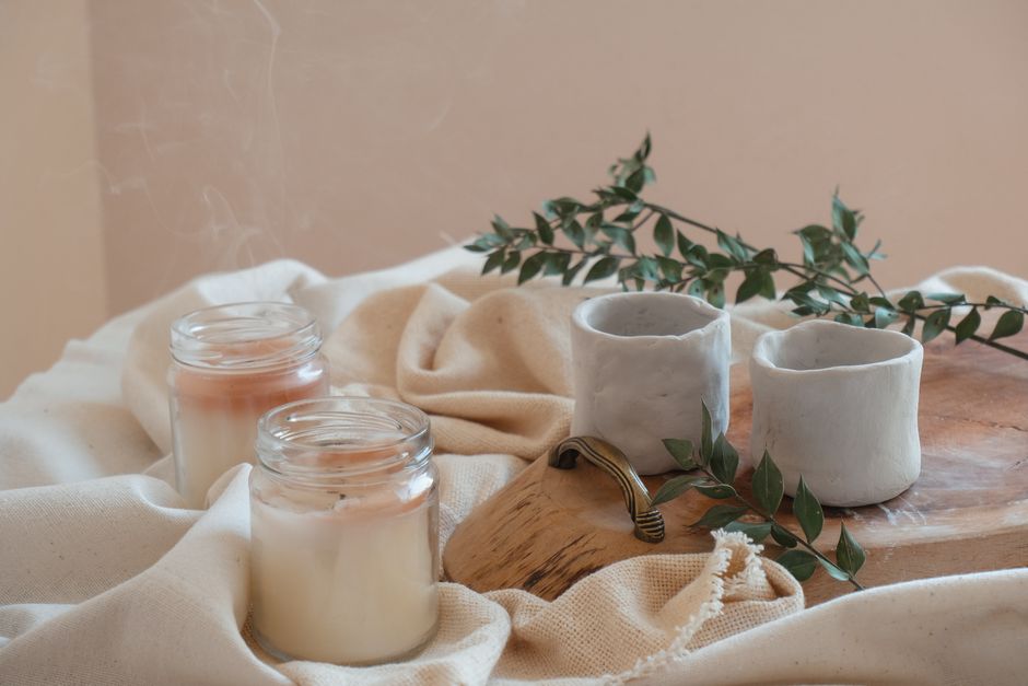 Stylish arrangement of artisanal candles, ceramic cups, and greenery on a rustic tray.