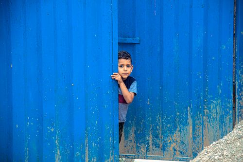 Free A curious child peeks through a vibrant blue door in Sari, Mazandaran Province, Iran. Stock Photo