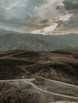Breathtaking aerial view of Qaladiza's mountainous terrain with a winding road under an overcast sky at sunset.