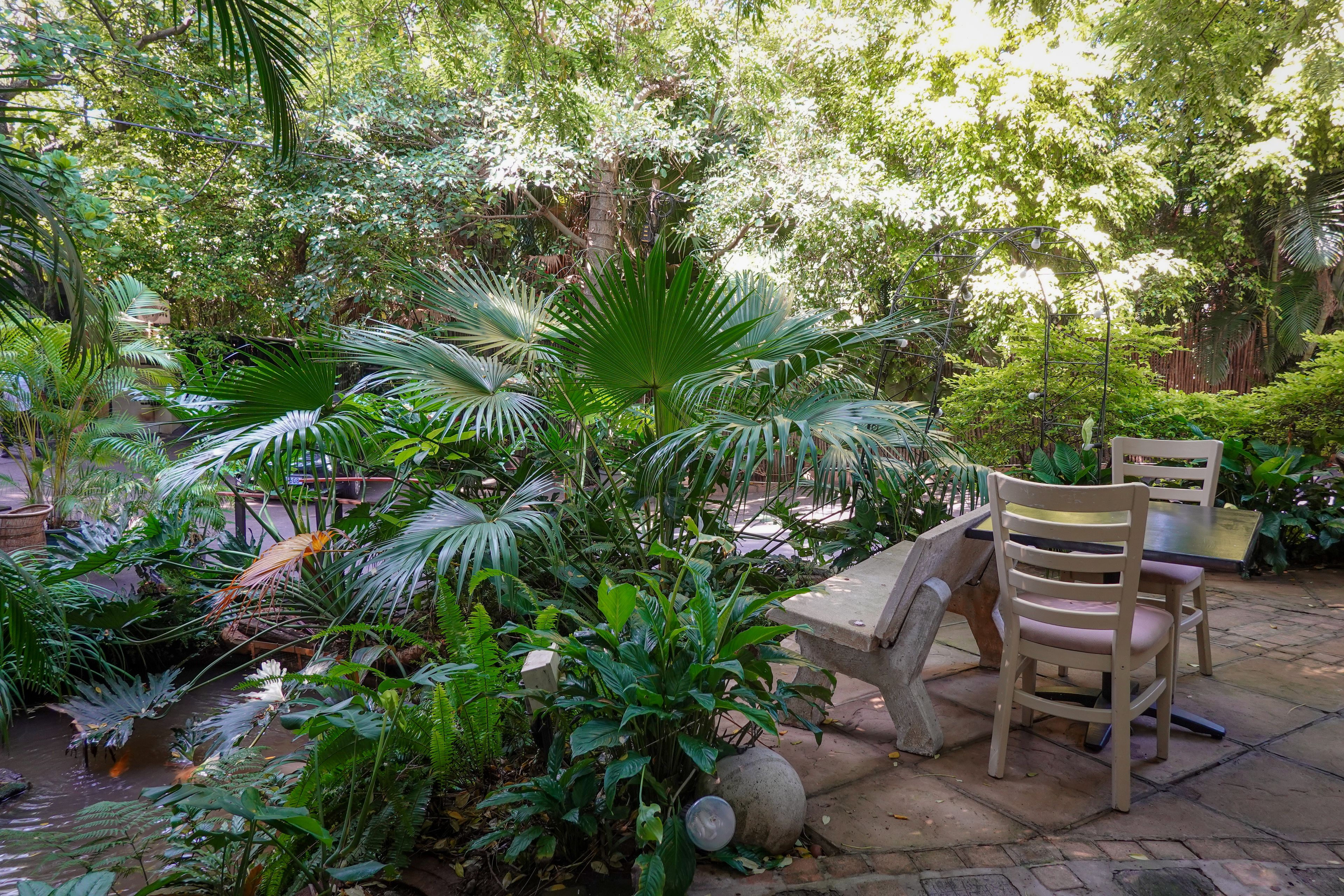 A lush tropical garden corner with outdoor table and chairs