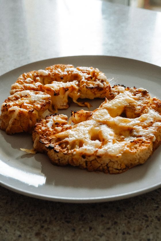 Two thick roasted cauliflower steaks with melted golden cheese and charred edges on a plate