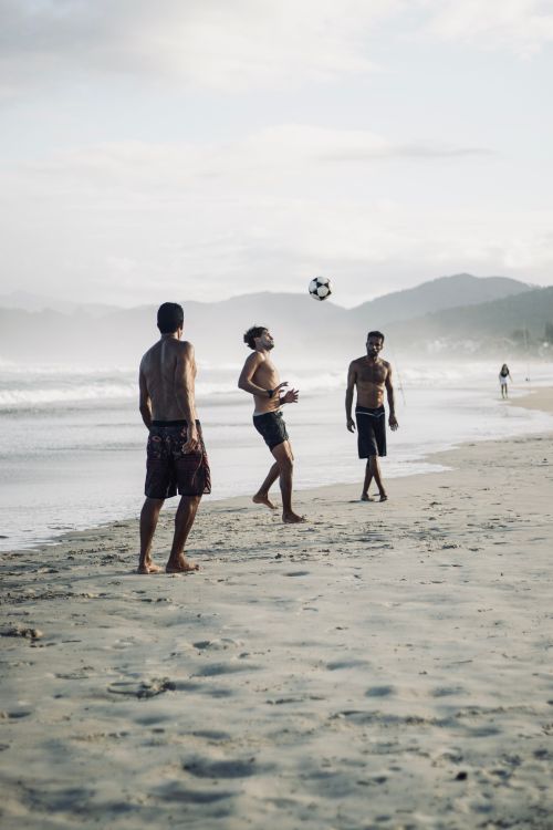 Free Three men enjoy a beach soccer game, showcasing leisure and friendship. Stock Photo
