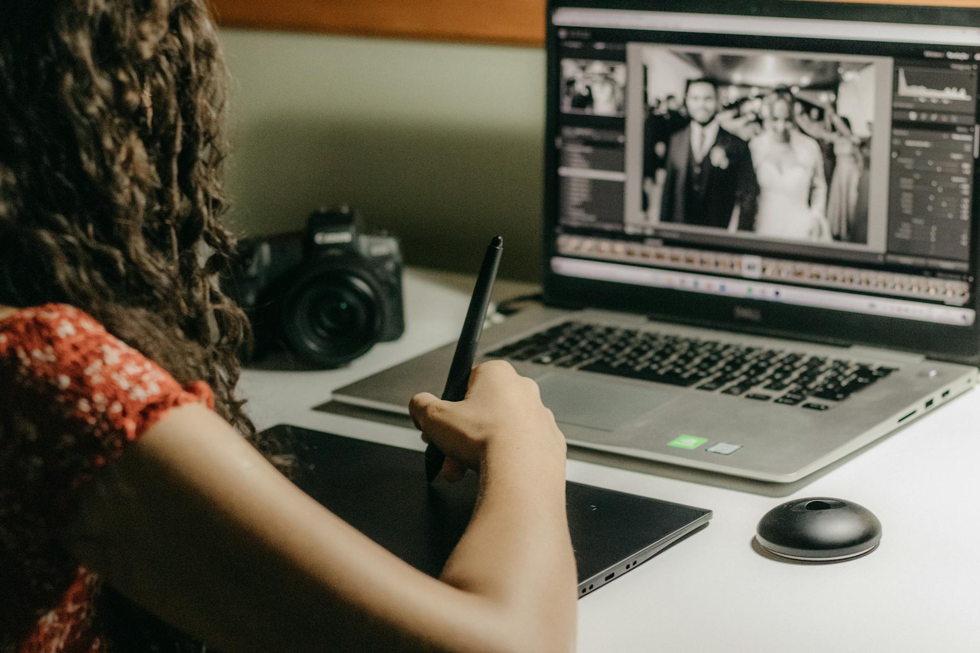 A woman editing wedding photos on a tablet using a laptop, representing modern graphic design work.