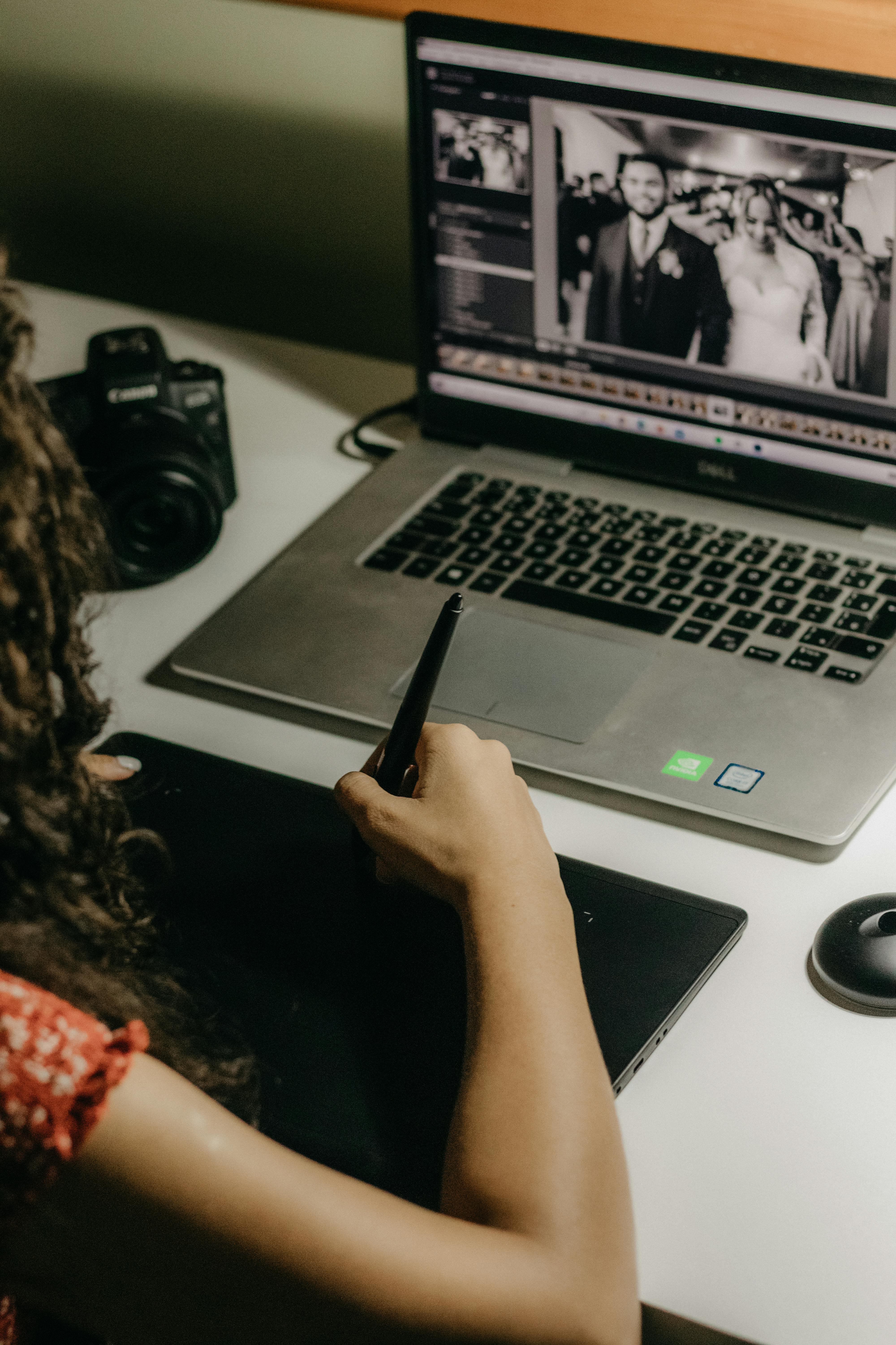 A graphic designer edits wedding photos on a laptop using a tablet for precision.