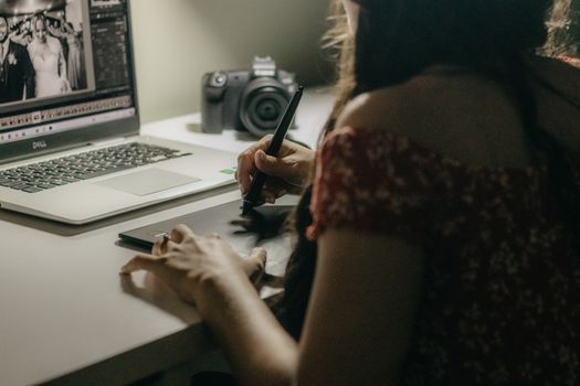A woman edits photos on a tablet and laptop in a creative workspace.
