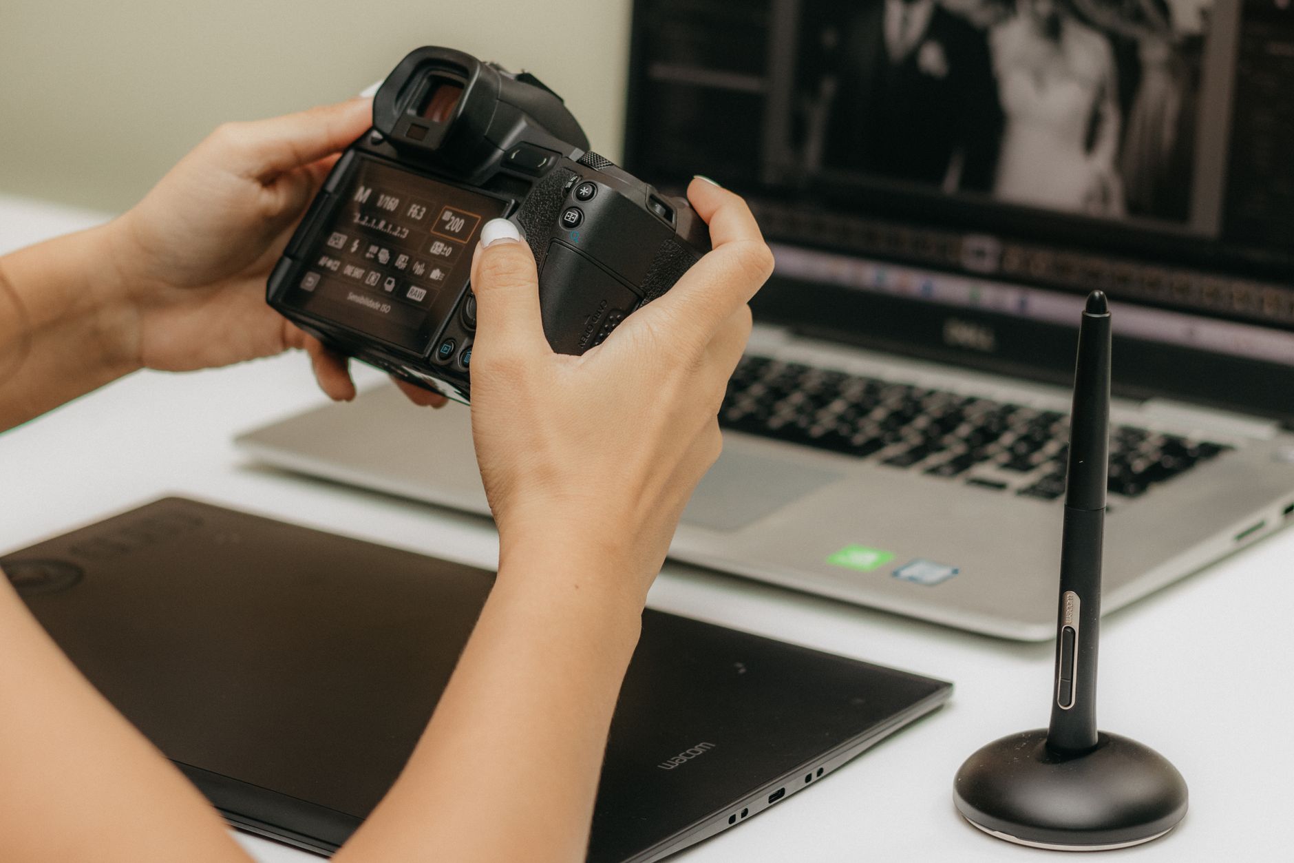 Close-up of hands using camera and laptop for photo editing.