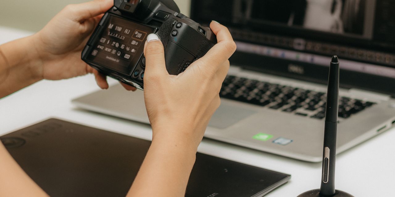 Close-up of hands using camera and laptop for photo editing.