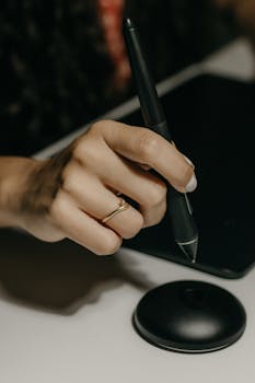 A woman's hand with a ring using a stylus on a digital tablet, focused close-up.