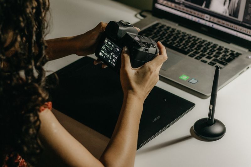 a photographer checking a camera back beside a laptop — photograph by Kawê Rodrigues on Pexels