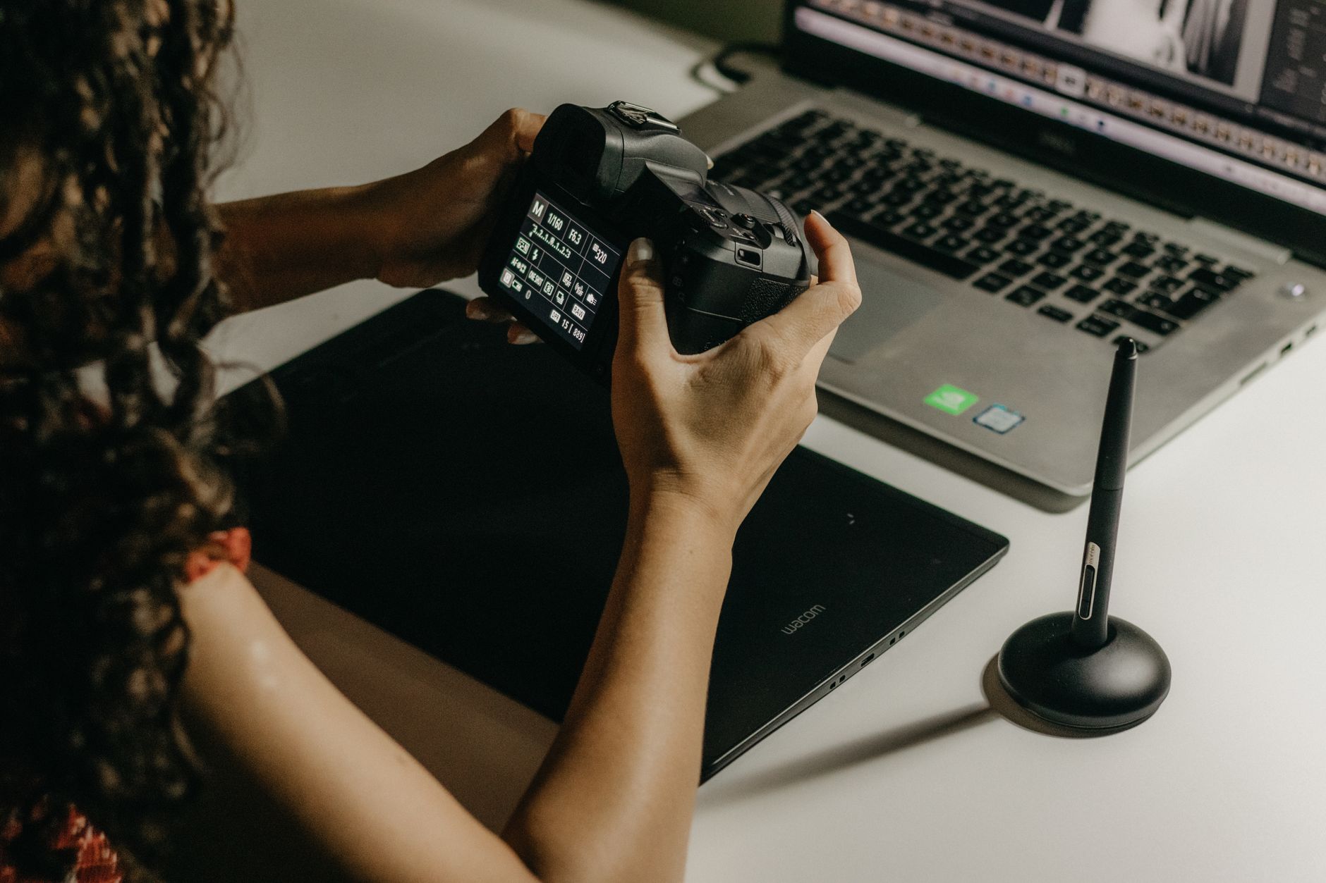 A woman reviews and edits her photos using a camera and laptop at a desk.