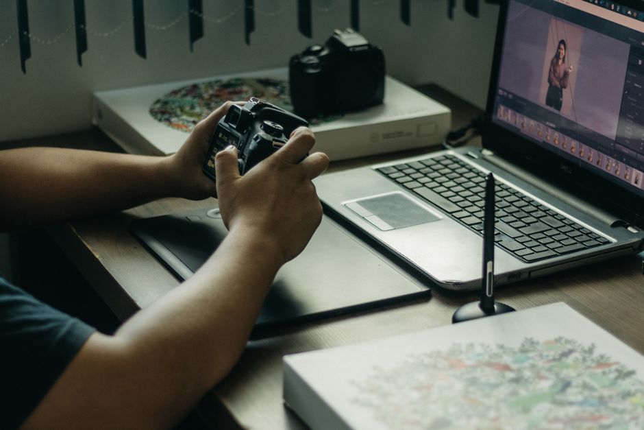 Can Someone Edit My Paper? Yes – Professional Editing in 2026 2 Photographer using a laptop and stylus for photo editing, holding a camera in an indoor setup.