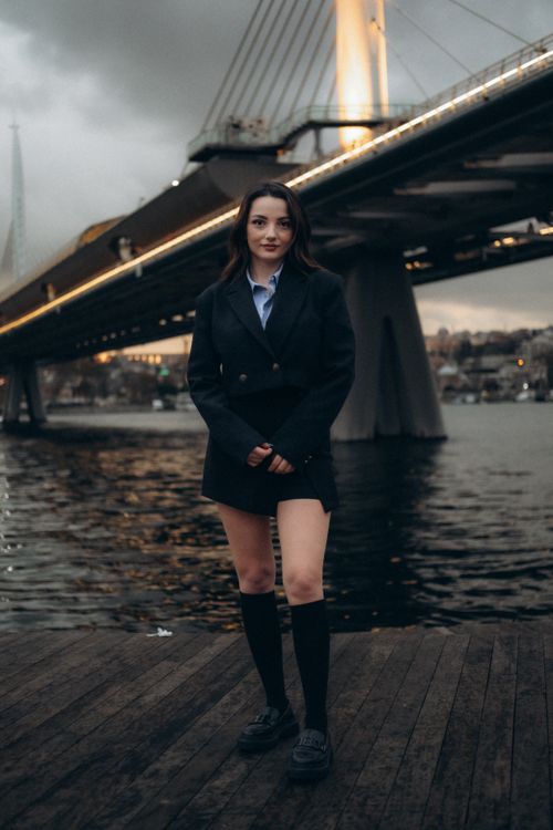 Free A fashionable woman poses near a lit bridge by the sea in Istanbul, Türkiye during the evening. Stock Photo